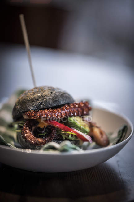Black burger with fried octopus and vegetables — Stock Photo