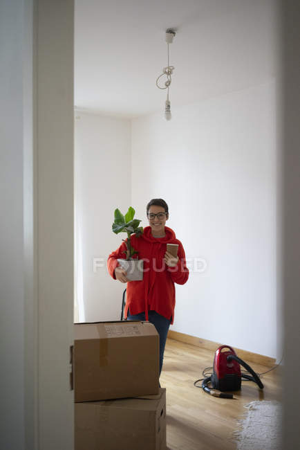Молода жінка переїжджає в свій новий дім, несучи насаджену рослину. — стокове фото
