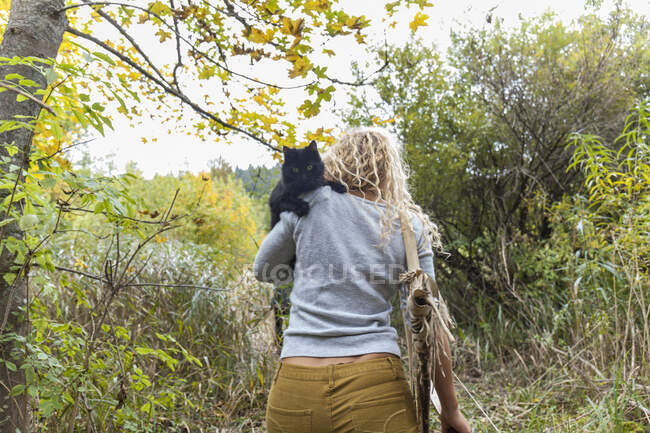 Visão traseira de arqueador com arco carregando gato preto em seu ombro na natureza — Fotografia de Stock
