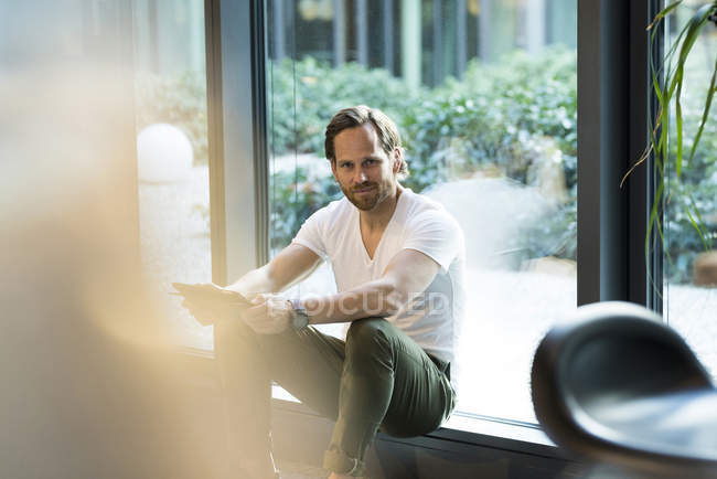 Homme d'affaires décontracté intelligent avec tablette assis devant la fenêtre dans un immeuble de bureaux moderne — Photo de stock