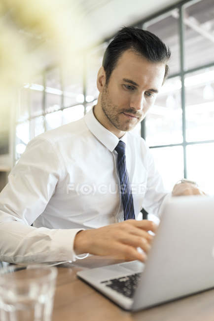 Giovane uomo d'affari che lavora su laptop in caffè su tavolo di legno — Foto stock
