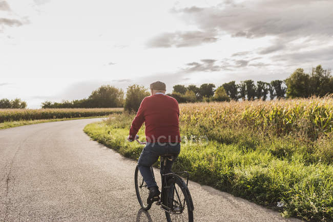 Senior man riding bicycle on country lane — Stock Photo