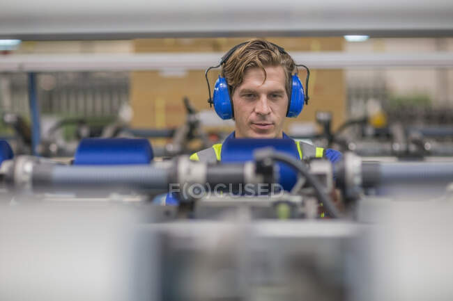 Hombre que usa la máquina de funcionamiento de los defensores del oído en fábrica - foto de stock
