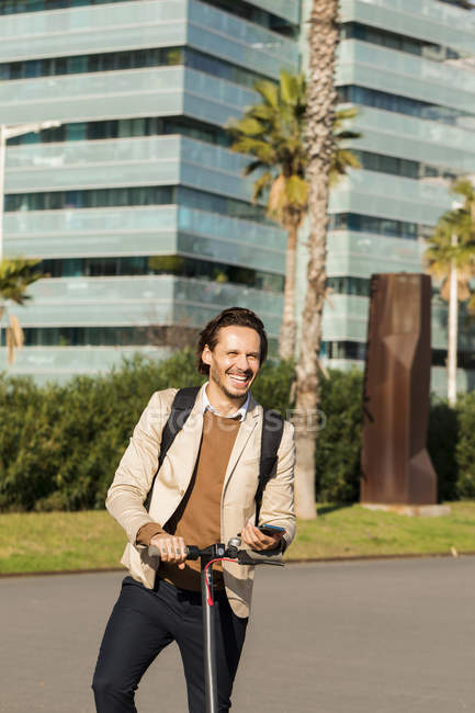 Retrato del hombre risueño con mochila y E-Scooter en la ciudad - foto de stock