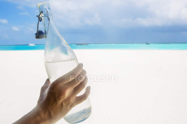 Maldivas, mano de mujer sosteniendo botella de agua en la playa - foto de stock