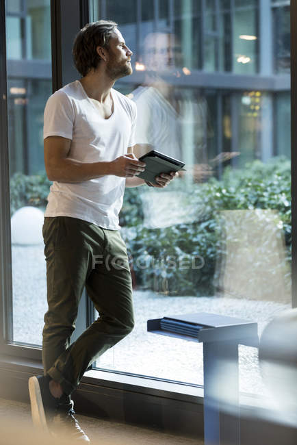 Homme d'affaires sensationnel avec tablette regardant à l'extérieur de la grande fenêtre dans un immeuble de bureaux moderne — Photo de stock