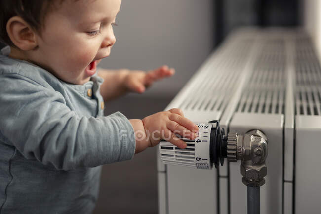 Bébé garçon excité jouant avec thermostat de chauffage — Photo de stock