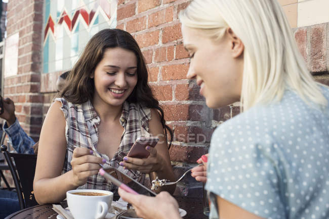 Two young women using cell phones at outdoor cafe — Stock Photo