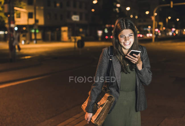 Riéndose joven mujer de negocios con bolsa de cuero en el teléfono por la noche - foto de stock