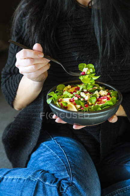 Woman eating mixed salad with lamb's lettuce, feta, pear, pomegranate ...