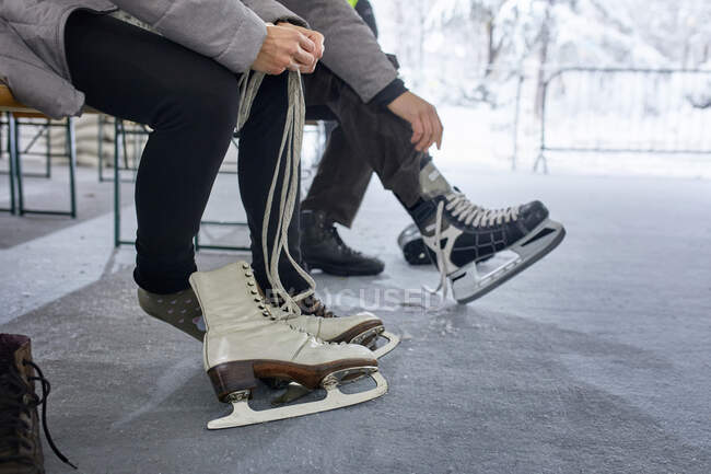 Couple assis sur le banc à la patinoire, mettre des patins à glace — Photo de stock