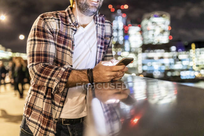 Ук, Лондон, зблизька людина, що спирається на поручні з мобільним телефоном з міськими вогнями на задньому плані — стокове фото