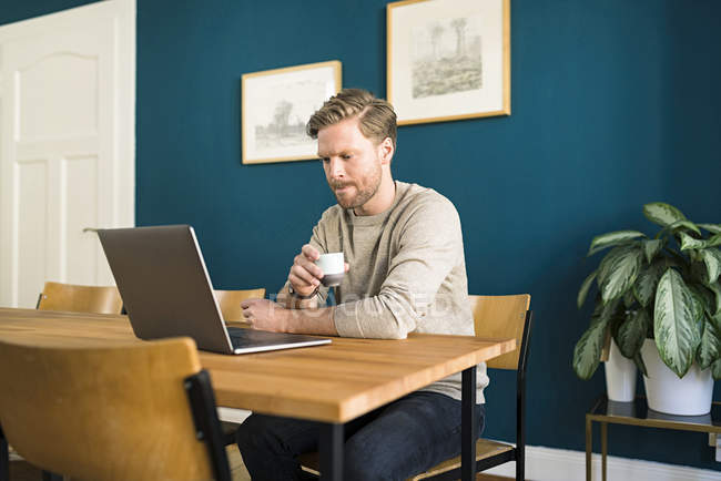 Homme travaillant sur ordinateur portable sur table en bois dans le bureau à la maison boire de l'espresso — Photo de stock