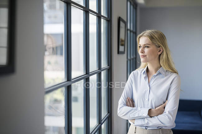 Confident businesswoman standing in office looking out of window — Stock Photo