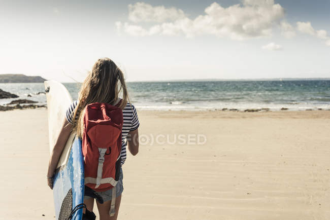 Junge Frau mit Rucksack, am Strand spazierend, mit Surfbrett — Stockfoto