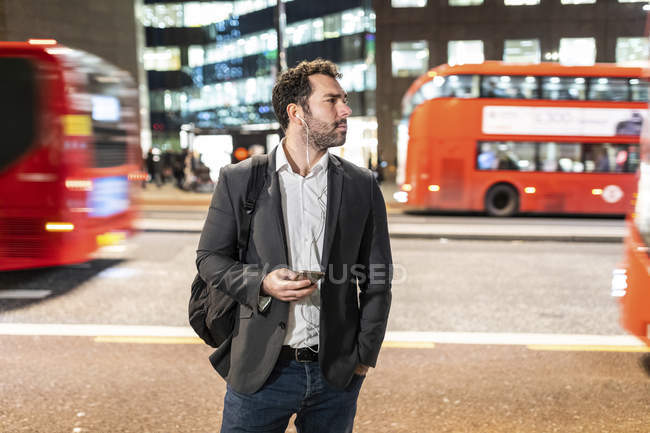 UK, London, businessman standing next to a busy street at night ...