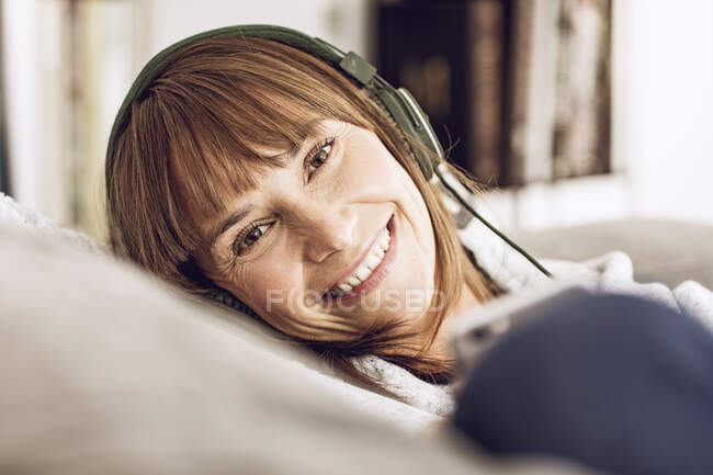 Женщина лежит на диване, слушая музыку в наушниках — стоковое фото