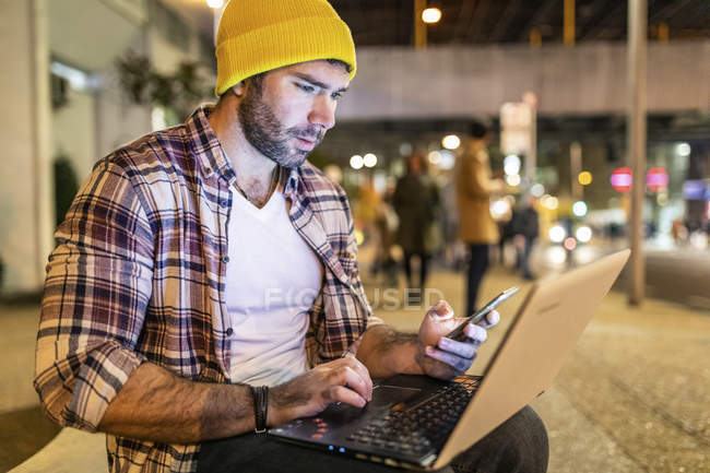Uk, london, mann mit telefon und laptop nachts in der stadt — Stockfoto