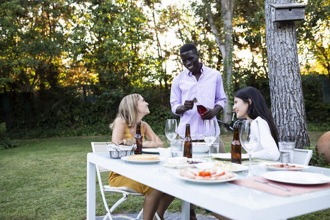 Amici a una cena estiva in giardino aprendo una bottiglia di vino — Foto stock