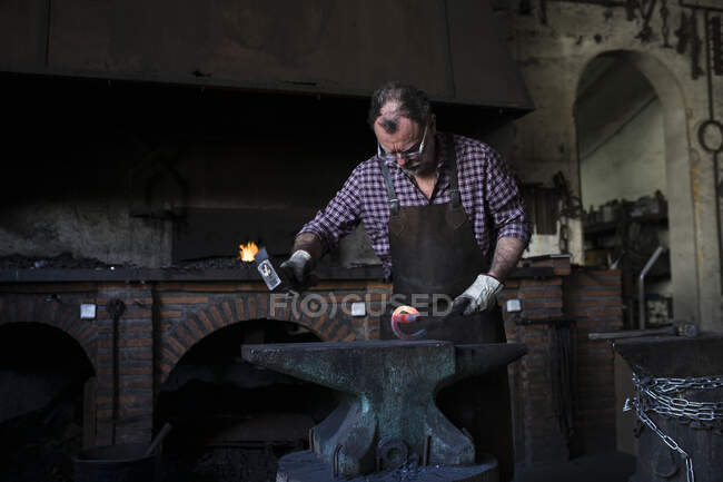 Schmied arbeitet mit Hammer am Amboss in seiner Werkstatt — Stockfoto