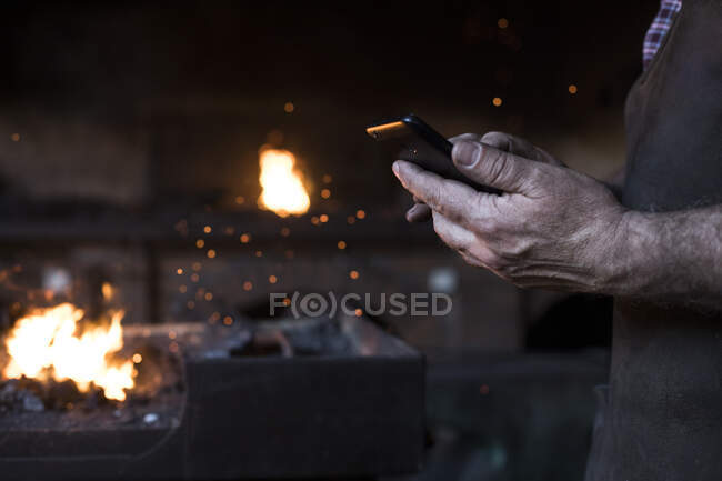 Close-up of blacksmith holding cell phone in his workshop — Stock Photo