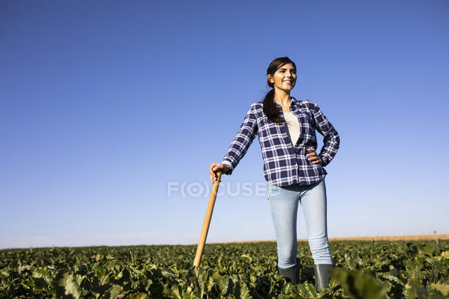 Jeune agricultrice avec houe sur le champ — Photo de stock