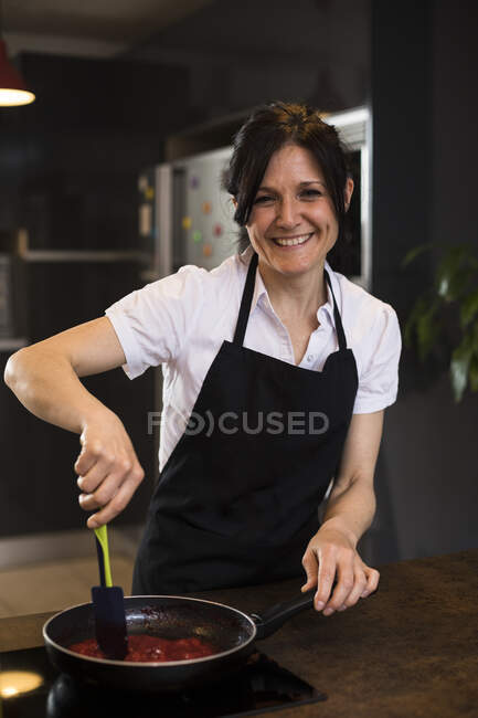 Portrait of smiling woman cooking in kitchen using a pan — Stock Photo