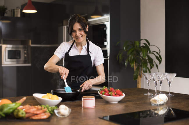 Портрет усміхненої жінки, яка готує їжу на кухні, за допомогою сковороди. — стокове фото