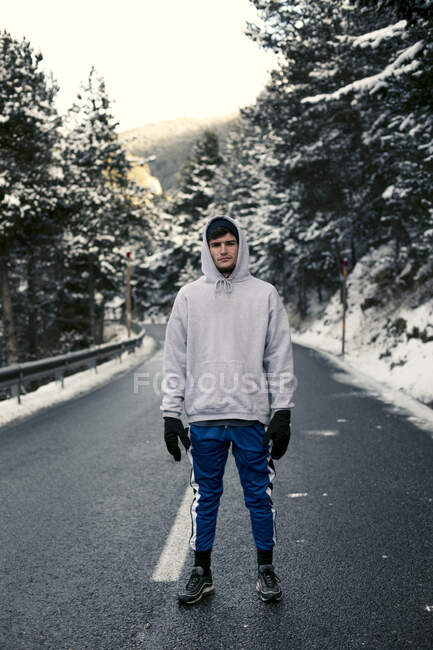 Молодой человек стоит на снежной дороге с деревьями на заднем плане — стоковое фото