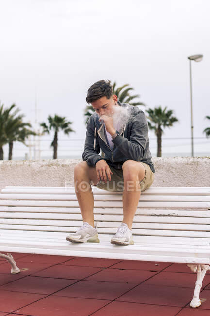 Молодий чоловік курить суглоб з пальмами на задньому плані. — стокове фото