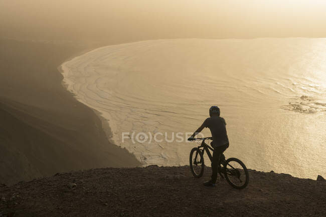 España, Lanzarote, ciclista de montaña en un viaje por la costa al atardecer disfrutando de la vista - foto de stock