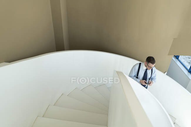Businessman using cell phone on stairs in modern office — Stock Photo