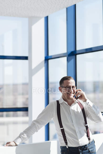 Щасливий бізнесмен розмовляє по мобільному телефону біля вікна в сучасному офісі. — стокове фото