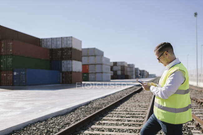 Людина на залізничних коліях перед вантажними контейнерами з використанням мобільного телефону — стокове фото