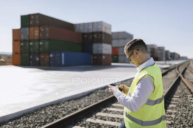 Hombre en vías férreas frente a contenedores de carga usando teléfono celular - foto de stock