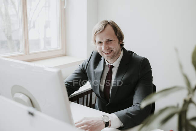 Portrait of smiling businessman using computer at desk in office — Stock Photo