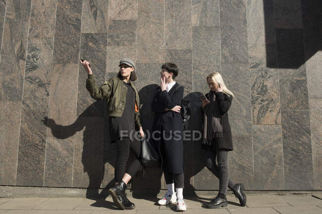 Drei junge Frauen stehen an einer Mauer in der Stadt und reden — Stockfoto