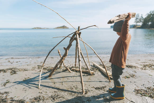 Ragazzo che gioca sulla spiaggia, costruendo un forte di legno alla deriva — Foto stock