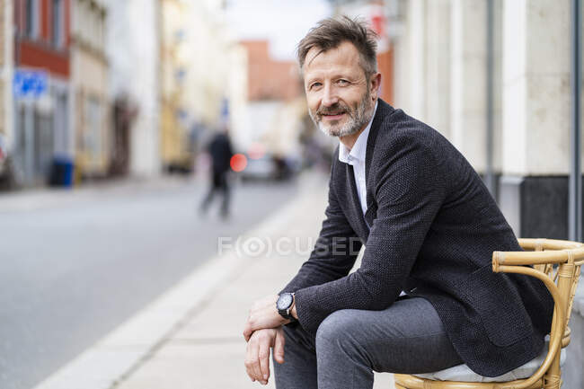 Ritratto di uomo d'affari maturo sorridente seduto su una sedia in città — Foto stock
