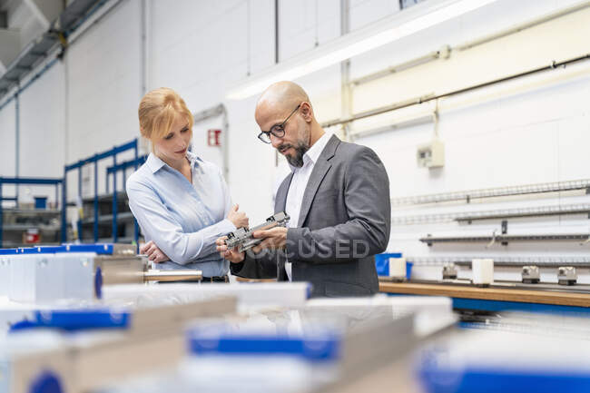 Homme d'affaires et femme d'affaires examinant la pièce dans l'usine — Photo de stock