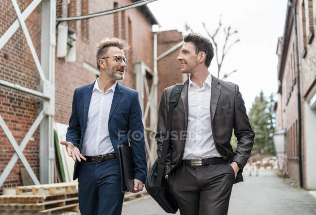 Deux hommes d'affaires souriants marchant et parlant dans un vieil immeuble en brique — Photo de stock