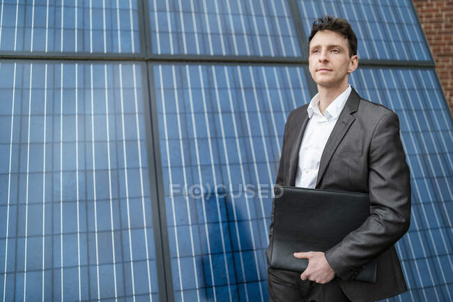 Бизнесмен держит папку, стоящую перед солнечными панелями — стоковое фото