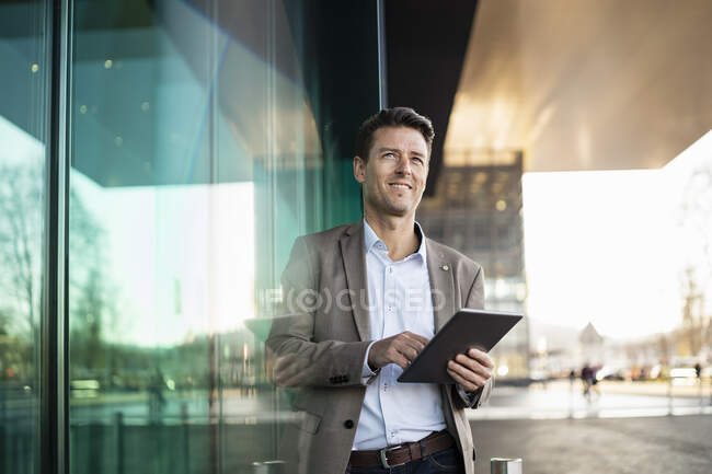 Hombre de negocios sonriente usando tableta fuera de un edificio en la ciudad - foto de stock
