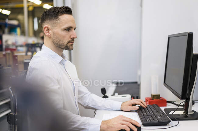 Empresario que usa la computadora en el escritorio en una fábrica - foto de stock