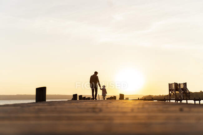 Germany, Bavaria, Herrsching, father and daughter walking on jetty at sunset — Stock Photo