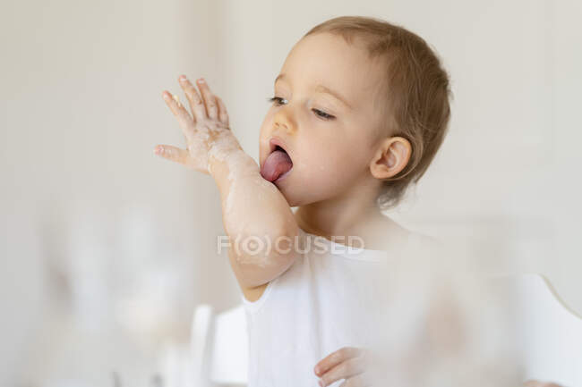 Bambina leccare il braccio mentre fa una torta in cucina a casa — Foto stock