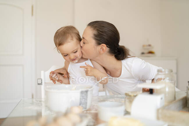 Мати цілує маленьку дочку, готуючи пиріг разом на кухні. — стокове фото