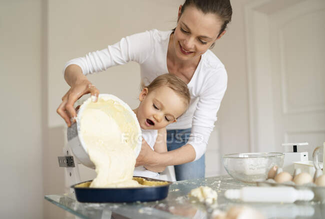 Mutter und kleine Tochter backen gemeinsam einen Kuchen und gießen Teig in Backform — Stockfoto