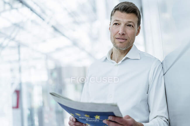 Businessman leaning against a wall reading newspaper — Stock Photo