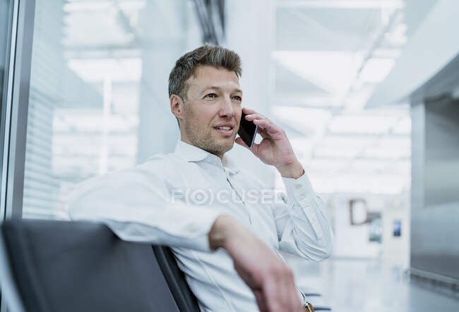 Businessman sitting in waiting area talking on cell phone — Stock Photo